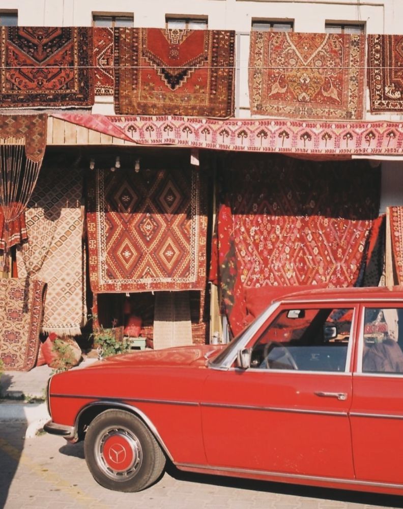 Vintage red Mercedes parked before hanging Persian rugs